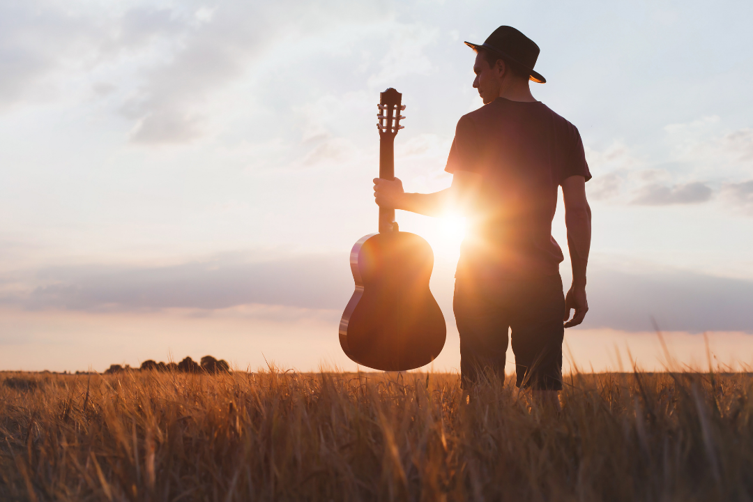 Man holding a guitar in a beautiful field